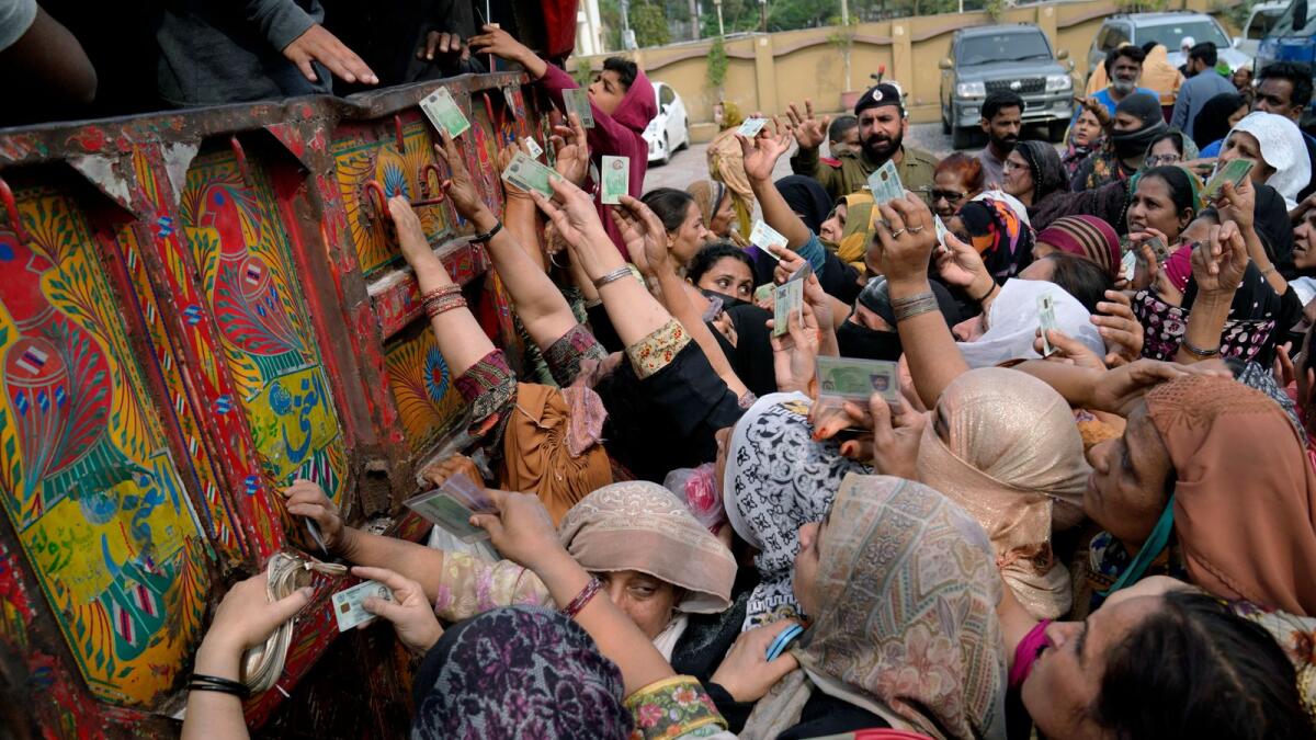 Women show their identity cards to receive a free sack of wheat flour at a distributing point in Lahore. — AP file