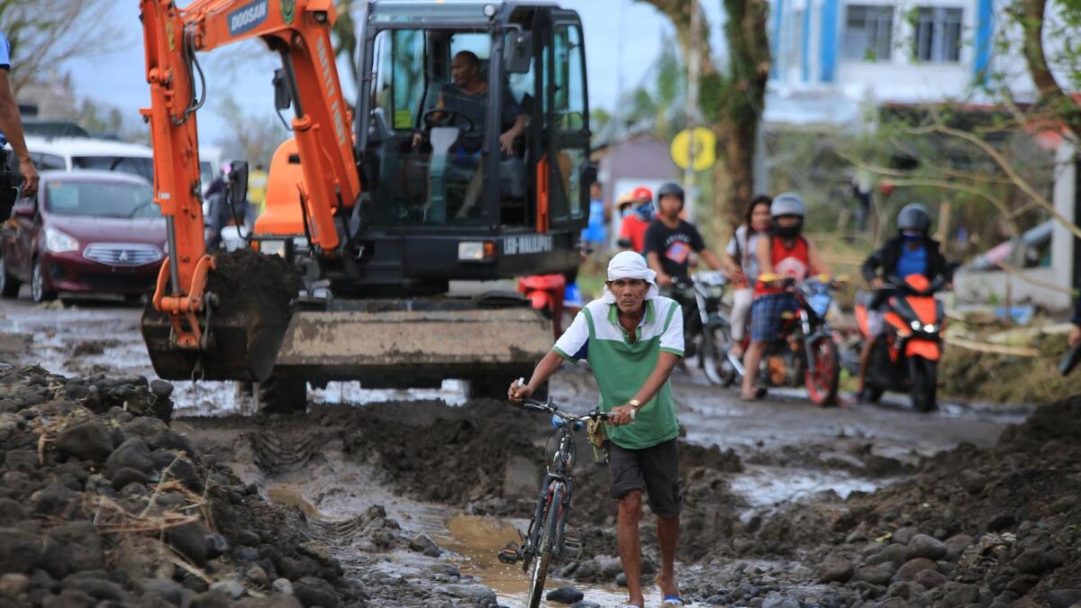 A man pushes his bike while a worker operates an excavator to clear a road of boulders and volcanic ash washed from nearby Mayon volcano brought by heavy rains during the super Typhoon Goni.