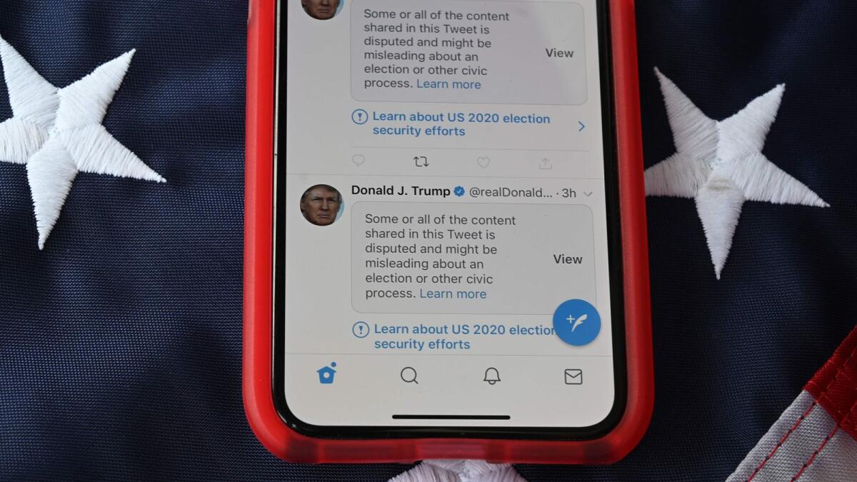 A mobile phone is seen placed on a US flag with Tweets from US President Donald Trump masked with warnings imposed by Twitter stating that they may be incorrect.
