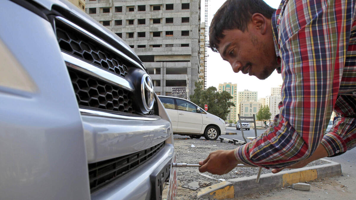 A worker puts a temporary export licence plate on a used car to shift it to the new used cars market in Al Ruqah Al Hamra. — Photos by M. Sajjad