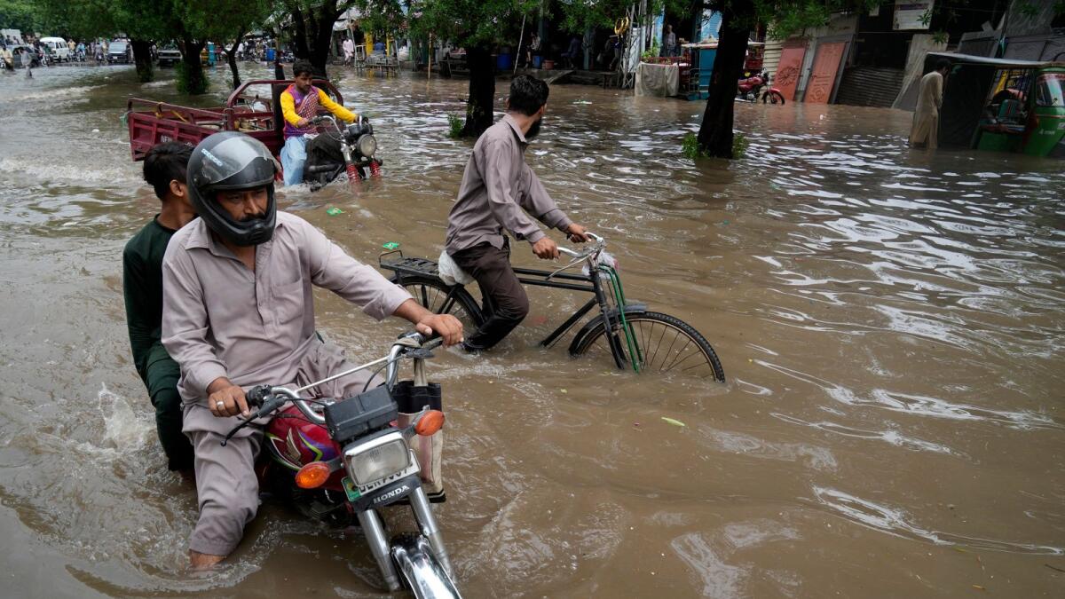 Motorcyclists drive through a flooded road caused by heavy rainfall, in Lahore, Pakistan, on Monday. An economic recovery has been hindered by floods last summer that killed 1,739 people and caused $30 billion in damage.  — AP