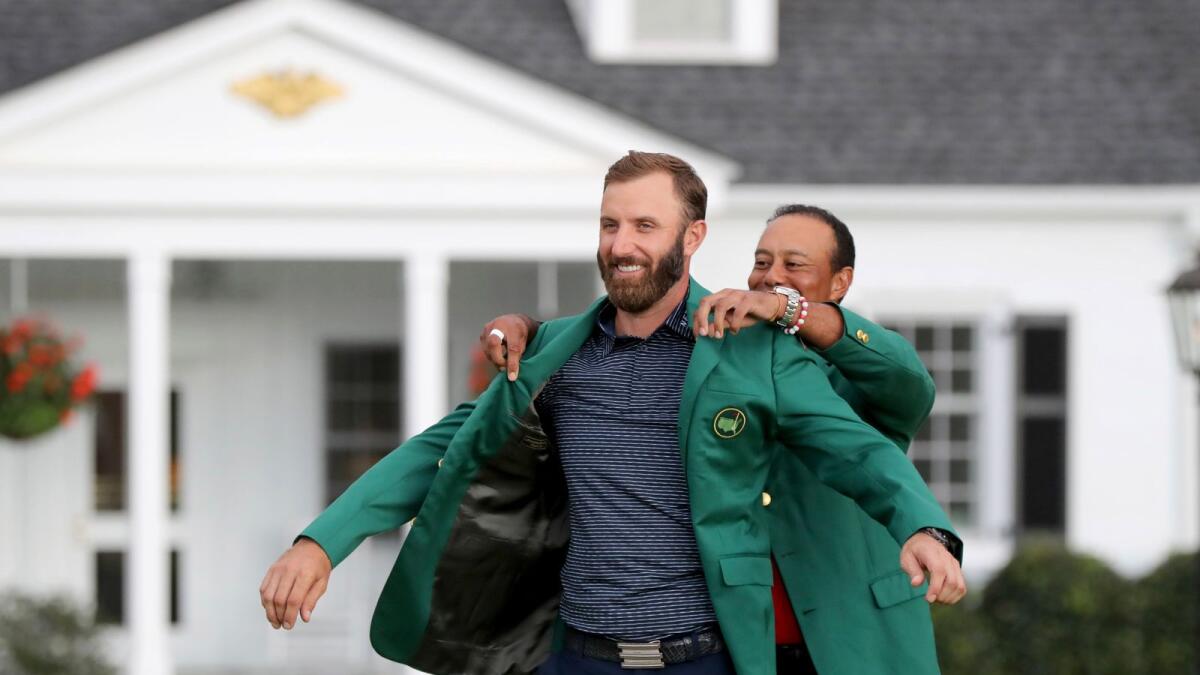 Last year's Masters champion Tiger Woods (right) presents Dustin Johnson his first green jacket after winning the Masters golf tournament.— AP