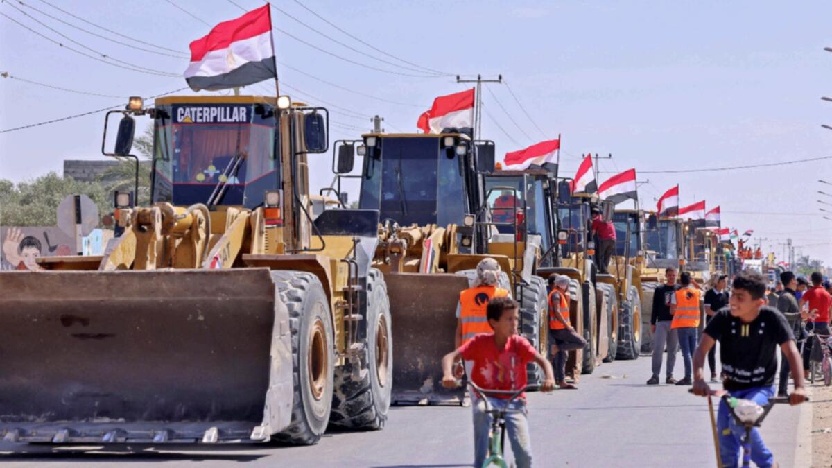 Palestinian boys cycle past a convoy of bulldozers provided by Egypt arriving at the Palestinian side of the Rafah border crossing between Egypt and the Palestinian Gaza Strip enclave. — AFP