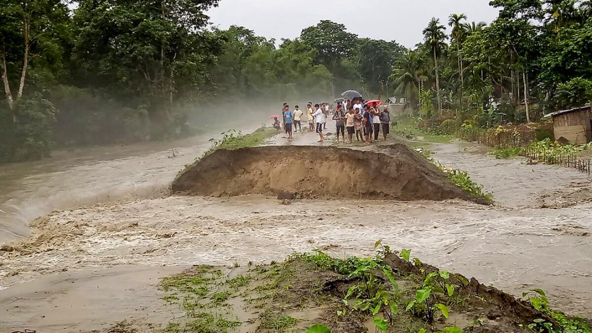 People stand near an embankment after it was washed away by floodwater during heavy rainfall, at Pathsala in Barpeta district, Assam, on Sunday, July 12, 2020. Photo: PTI