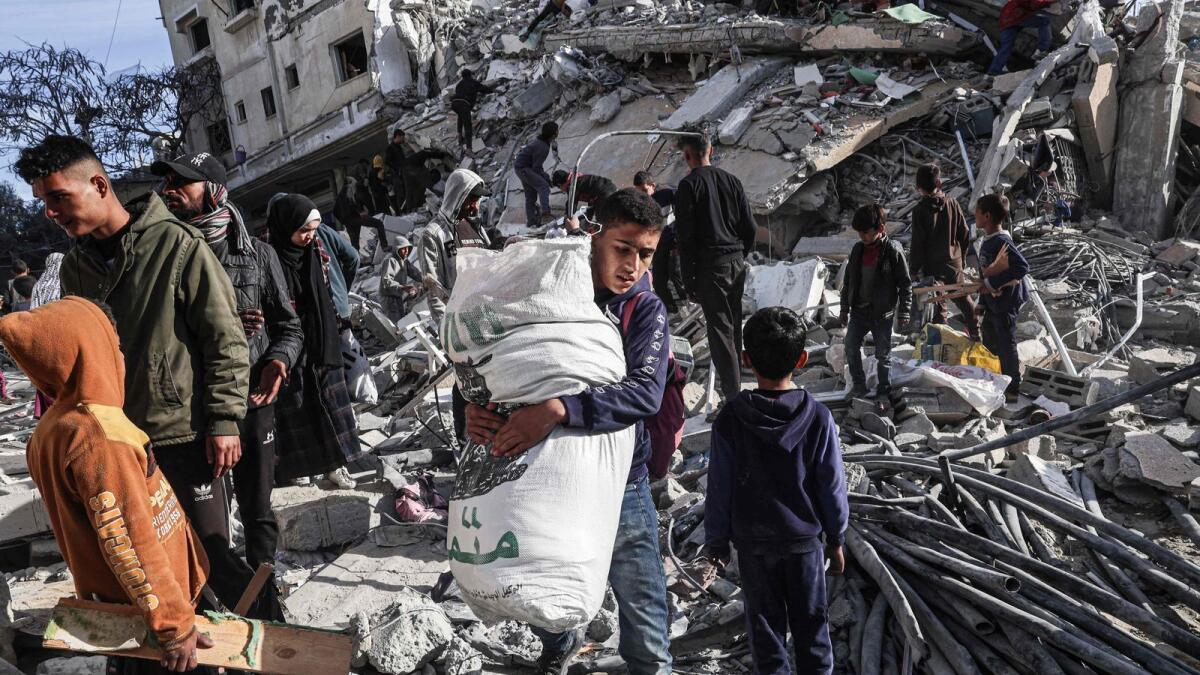 A Palestinian youth walks away with some items salvaged from the rubble of a residential building hit in an overnight Israeli air strike in Rafah. — AFP