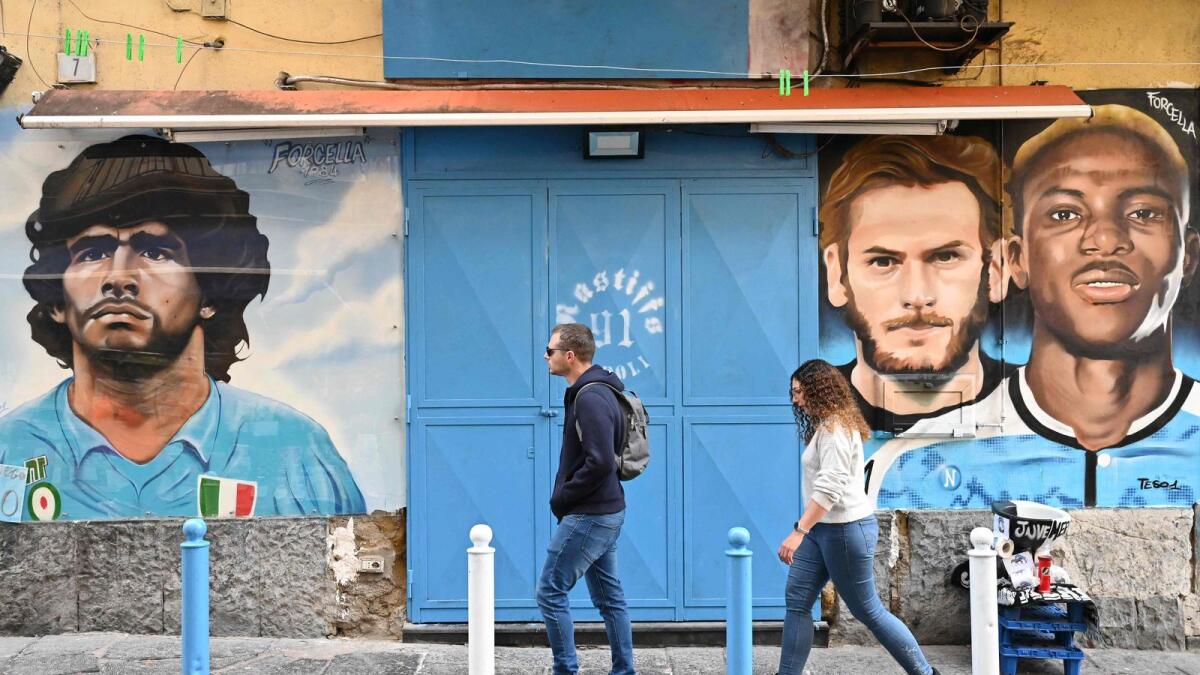 People walk past a murals depicting late football icon Diego Maradona, current Napoli  stars Khvicha Kvaratskhelia, and Victor Osimhen in the Forcella district in Naples. — AFP