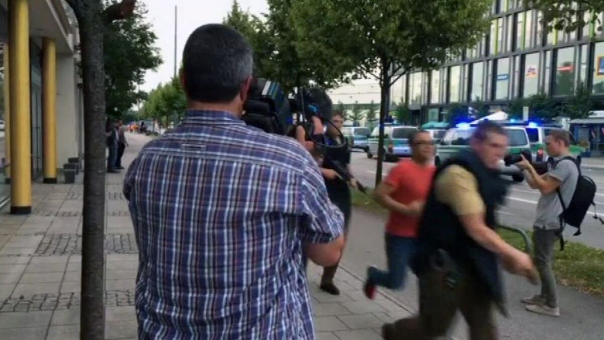Armed police move past on looking media responding to a shooting at a shopping center in Munich, Germany