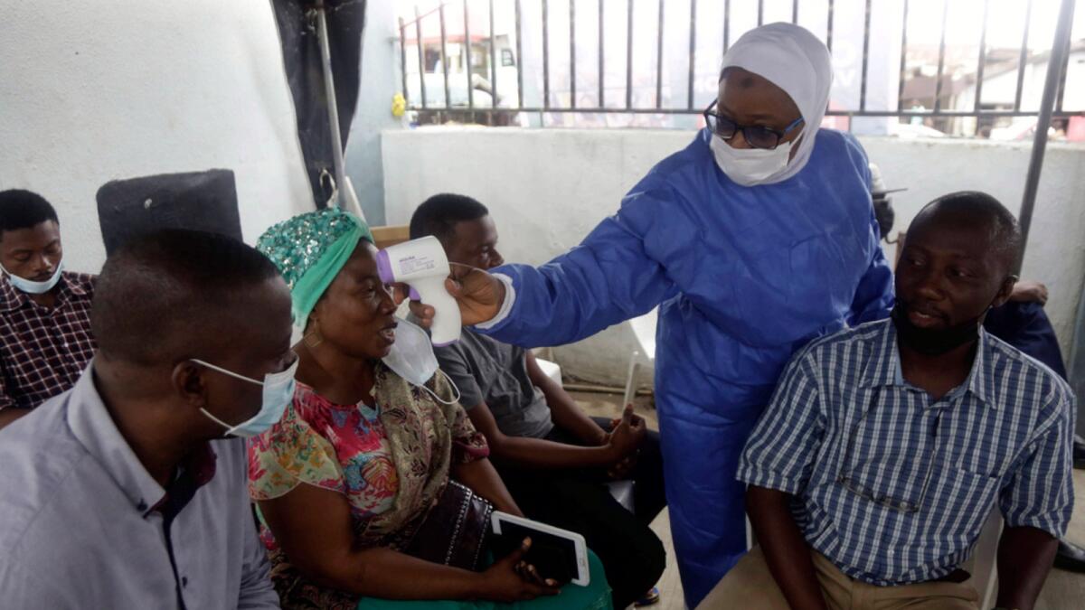 A nurse in protective gear takes temperature of people waiting to take Cov id-19 vaccine at a health centre in Lagos. — AP