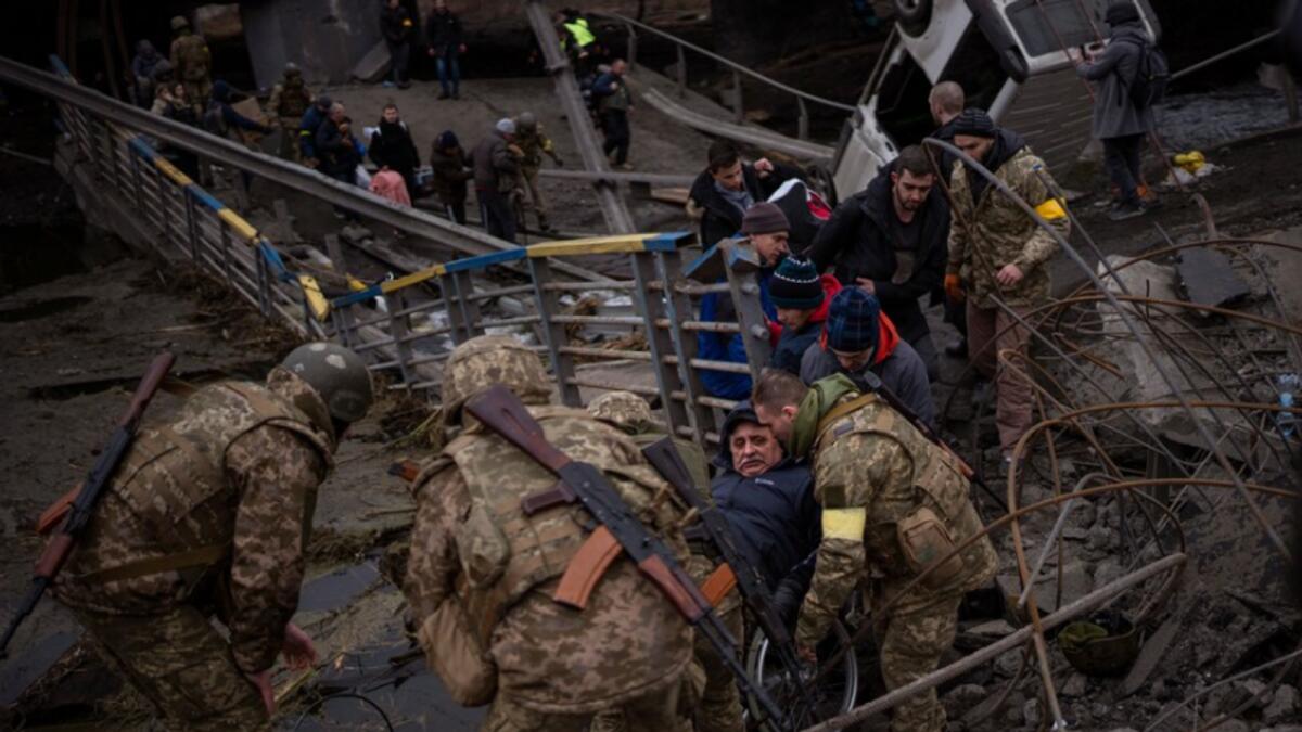 Ukrainian soldiers help a man on a wheelchair as people try to flee crossing the Irpin river in the outskirts of Kyiv, Ukraine, Saturday, March 5, 2022. Photo: AP