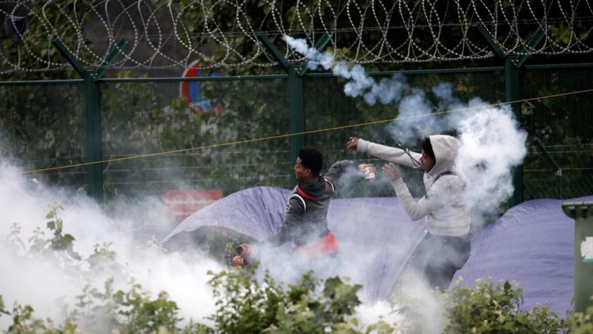 Migrants throw objects at French police officers in a cloud of tear gas as police dismantle a makeshift shelter camp in Calais, France. Photo: Rueters
