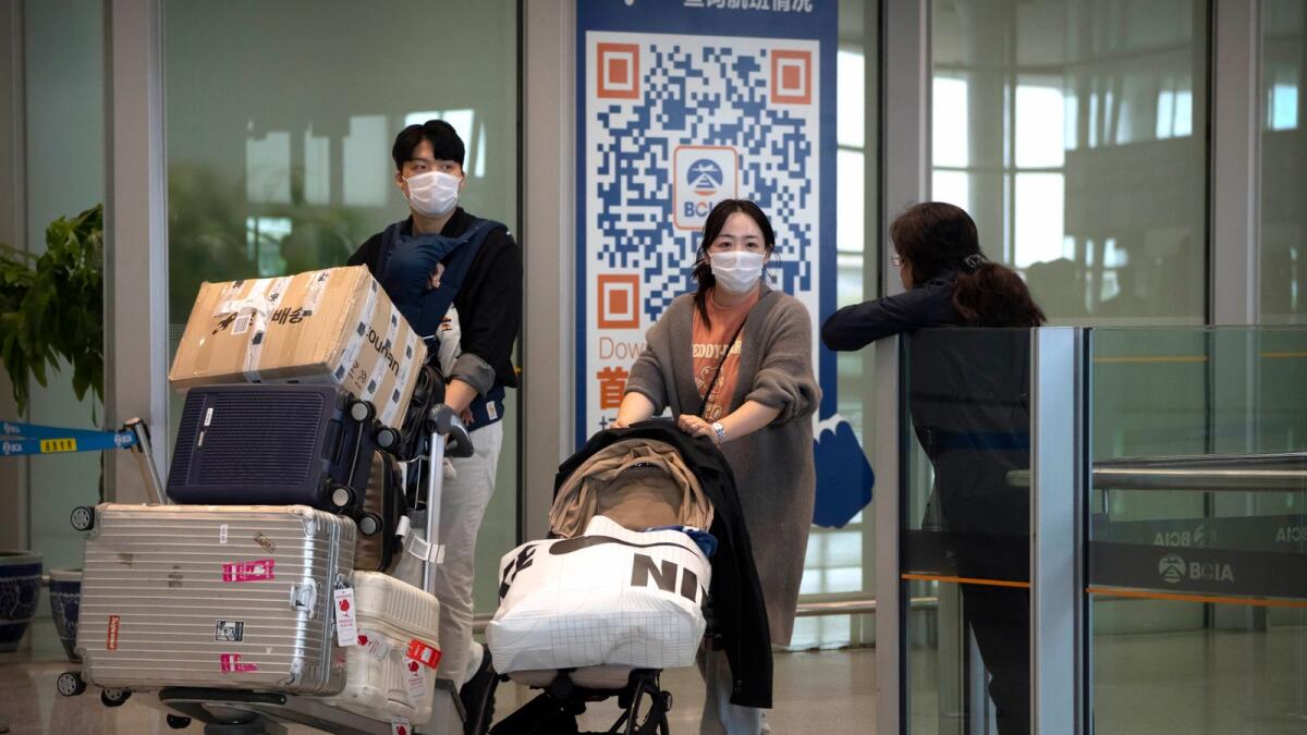Travellers wearing face masks walk through the international flight arrivals area at Beijing Capital International Airport in Beijing on Wednesday. — AP