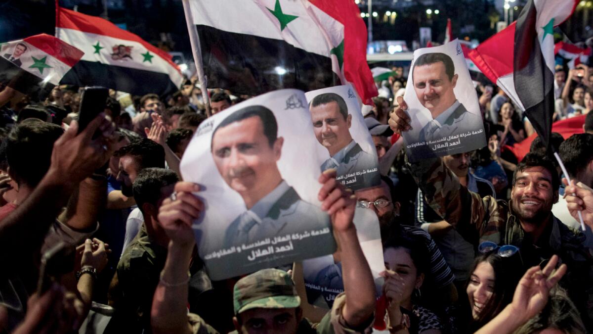 Supporters of Syrian President Bashar Assad hold up national flags and the leader's pictures as they celebrate in Damascus. Photo: AP