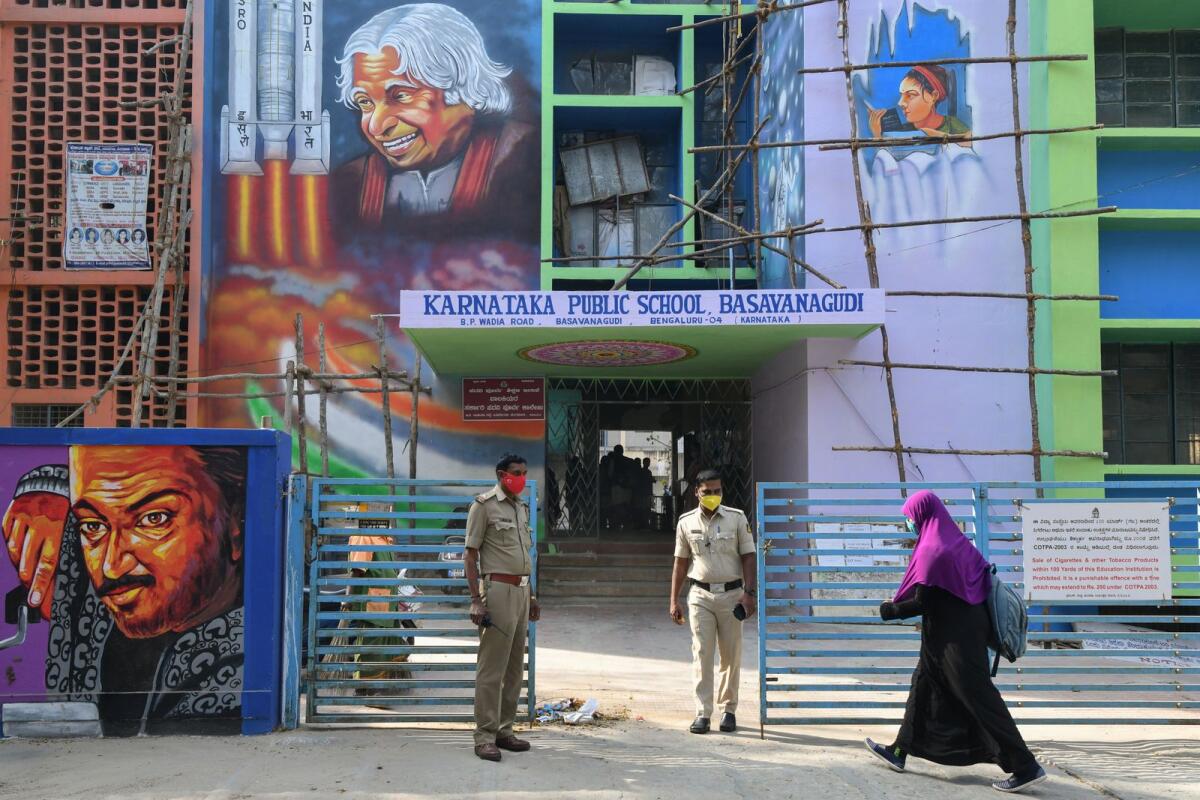 Police stand guard as a student of a government high school and pre-university college for women enters the premises of the educational institute in Bangalore on February 16, 2022, after schools reopened in southern India under tight security after authorities banned public gatherings following protests over Muslim girls wearing the hijab in classrooms. Photo: AFP