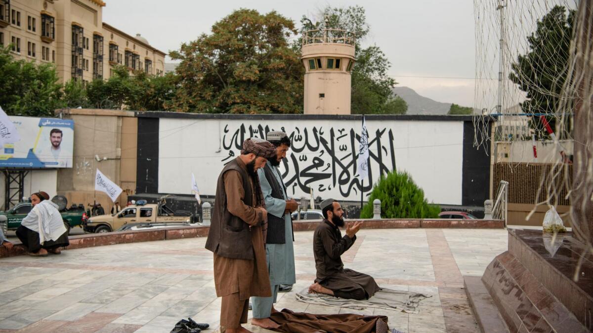 Taliban fighters pray in Masood Square, just outside Kabul's Green Zone, and in front of what used to be the American embassy. Walking its streets a year ago was like wandering into the modern ruins of another empire come and gone from Afghanistan. Now, the Taliban have adopted it as their own. (Kiana Hayeri/The New York Times)