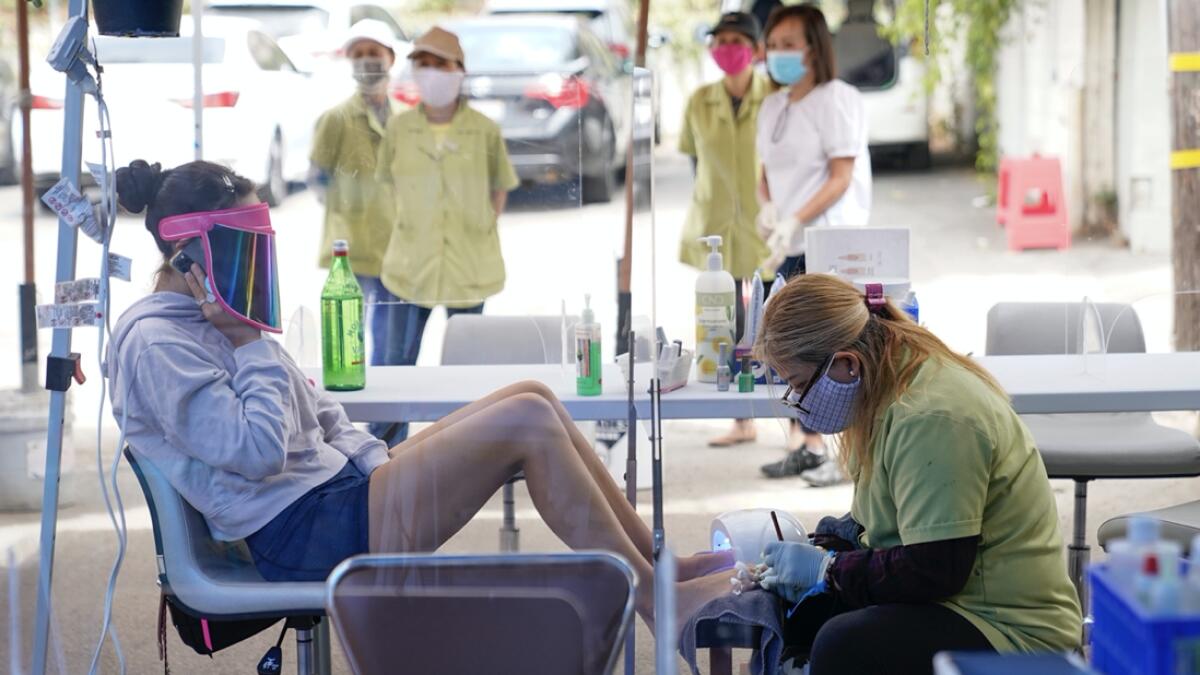 Tyson Salomon, left, gets a pedicure outside Pampered Hands nail salon, in Los Angeles. The salon is allowed to operate outside. California's confirmed coronavirus cases have topped 409,000, surpassing New York for most in the nation. Photo: AP