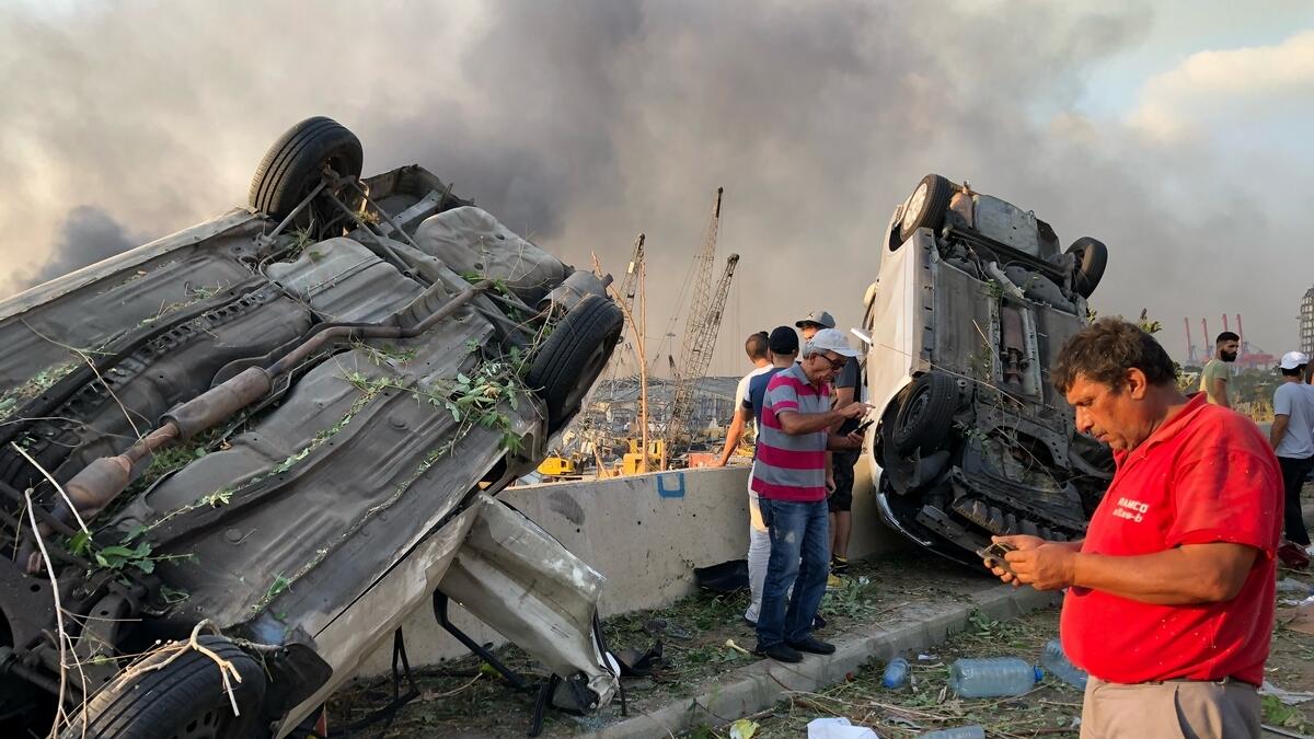 People stand near damaged cars following an explosion in Beirut. Reuters