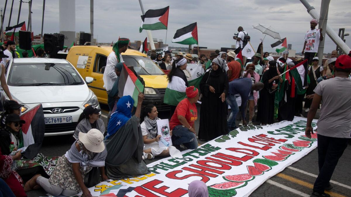 Pro-Palestinian activists holds a banner while they sit down for a moment while marching from Mary Fitzgerald Square towards Nelson Mandela Bridge during a pro-Palestinian demonstration by various political parties and trade unions in Johannesburg. (Photo: AFP)
