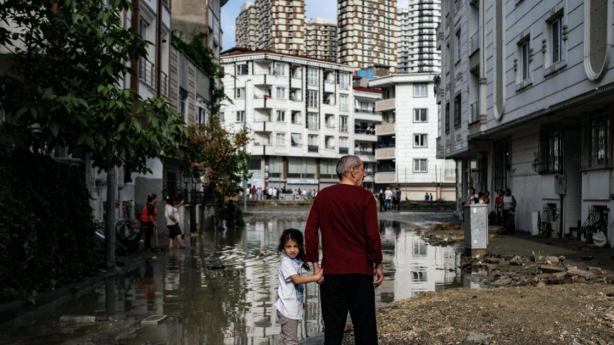 A man and a child stand in a flooded street in the Esenyurt district of Istanbul where at least one person died as heavy rains and hail storms lashed Istanbul, Turkey. Photo: AFP