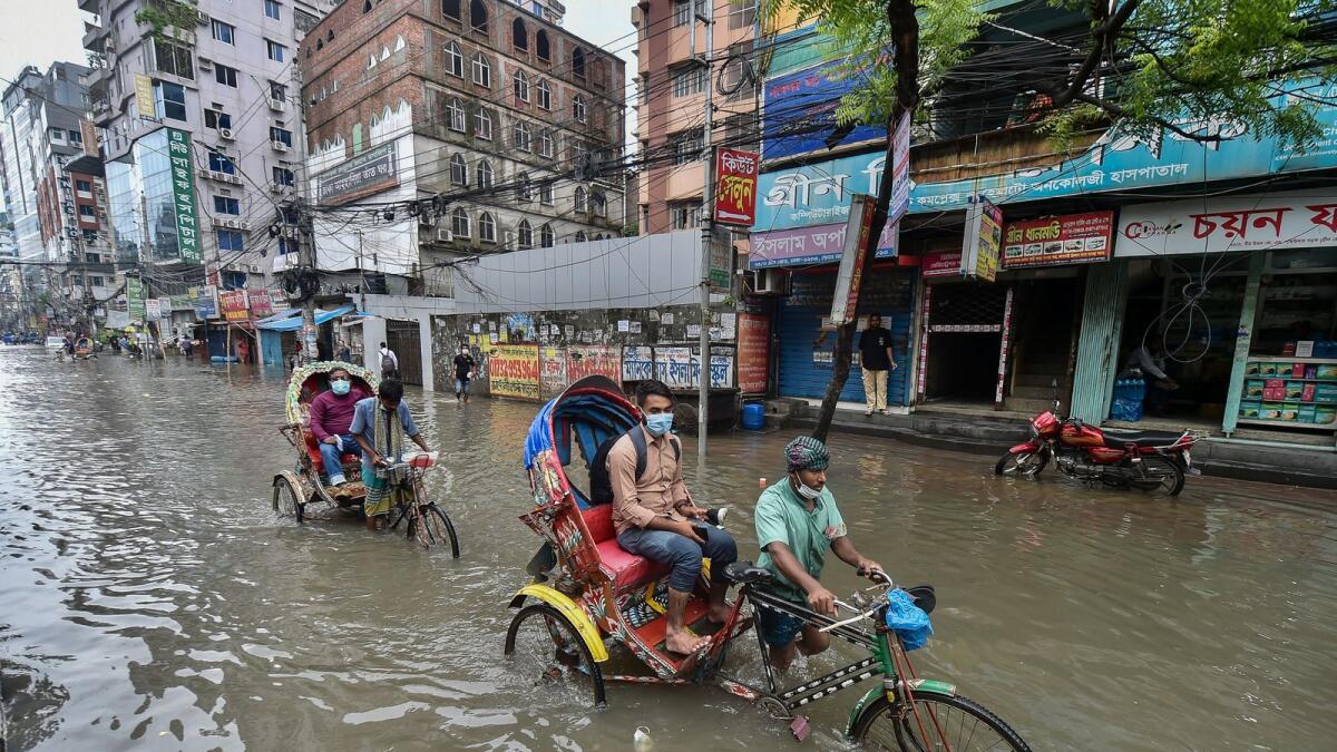 Cycle rickshaw pullers wade through a flooded street after heavy rains in Dhaka. Photo: AFP