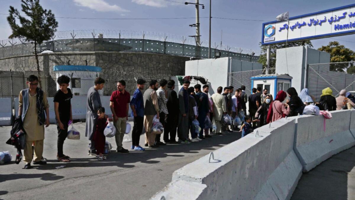Afghans, hoping to leave Afghanistan, queue at the main entrance gate of Kabul airport. — AFP