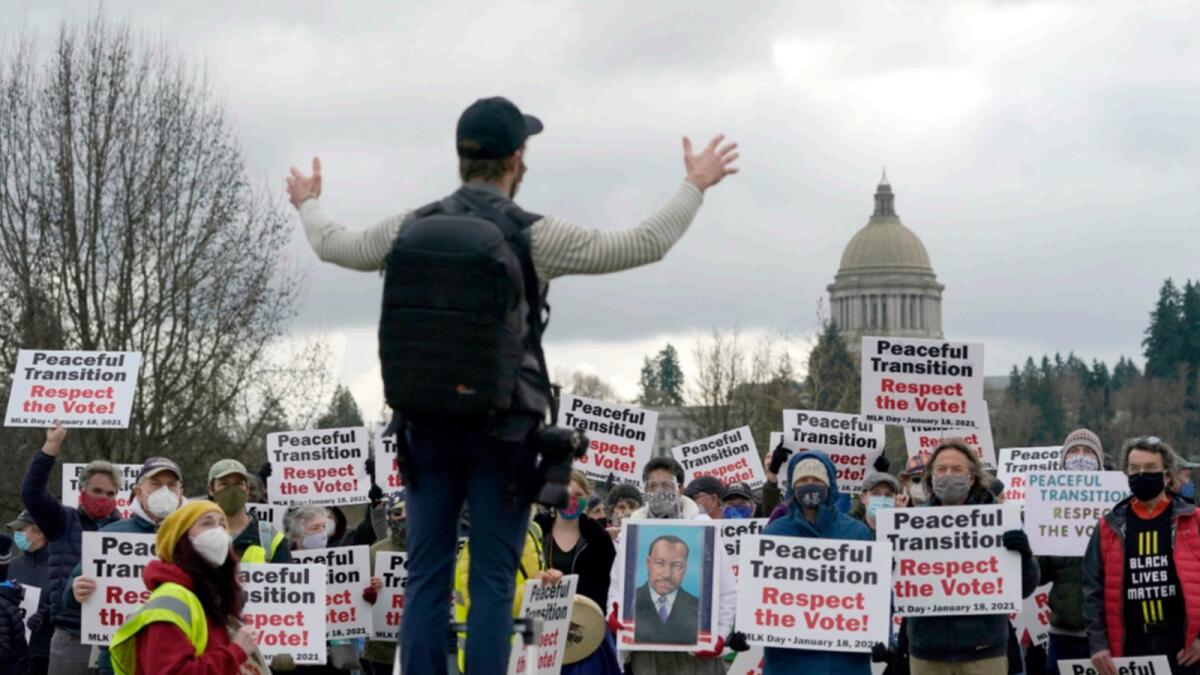 People hold signs as they assemble for a group photo following a vigil supporting a peaceful transition from Donald Trump to Joe Biden in Olympia. More than 100 people took part in the demonstration ahead of Biden's upcoming inauguration on Wednesday. — AP