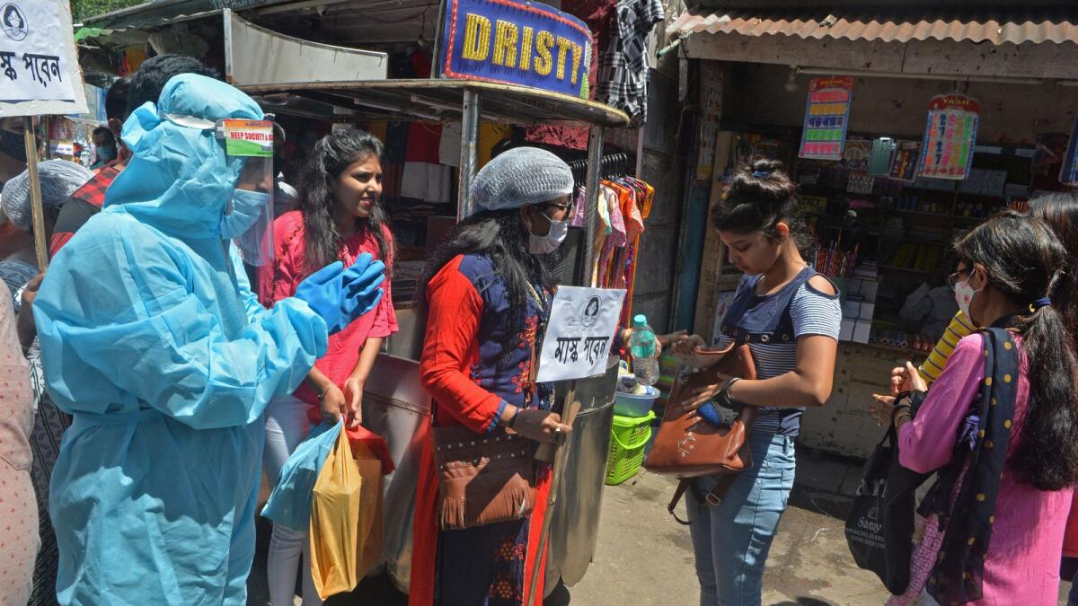 A volunteer wearing protective gear urges people in a market to wear facemasks as part of an awareness drive against the spread of Covid-19 in India. Photo: AFP