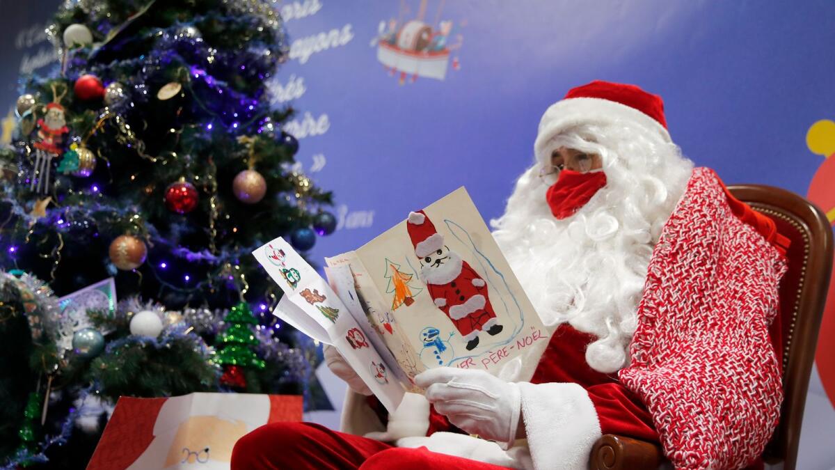 A postal worker dressed as Santa, reads letters to addressed to 'Pere Noel' - Father Christmas in French -  decorated with love hearts, stickers and glitter, in Libourne, southwest France.
