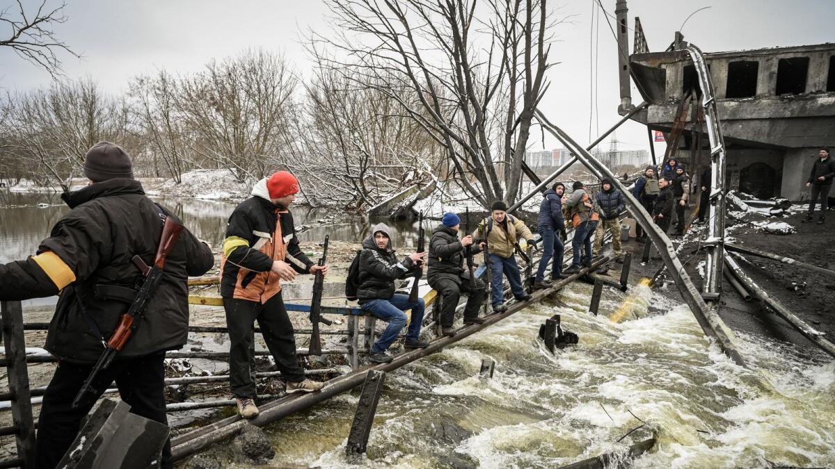 Members of a Ukrainian civil defense unit pass new assault rifles to the opposite side of a blown up bridge on Kyiv’s northern front on March 1, 2022. Photo: AFP