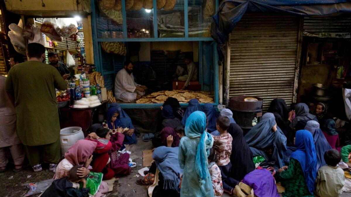 Afghan women and children sit in front of a bakery waiting for bread donations in Kabul's Old City. — AP