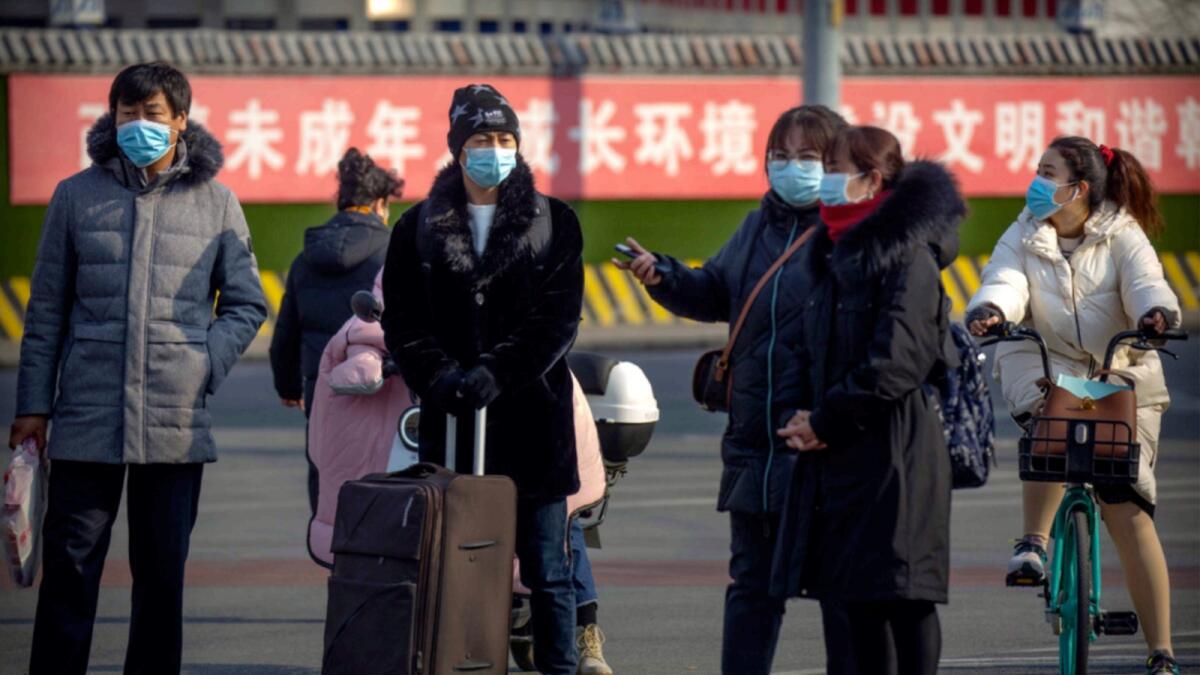 People wearing face masks to protect against the spread of the coronavirus wait to cross an intersection in Beijing. — AP