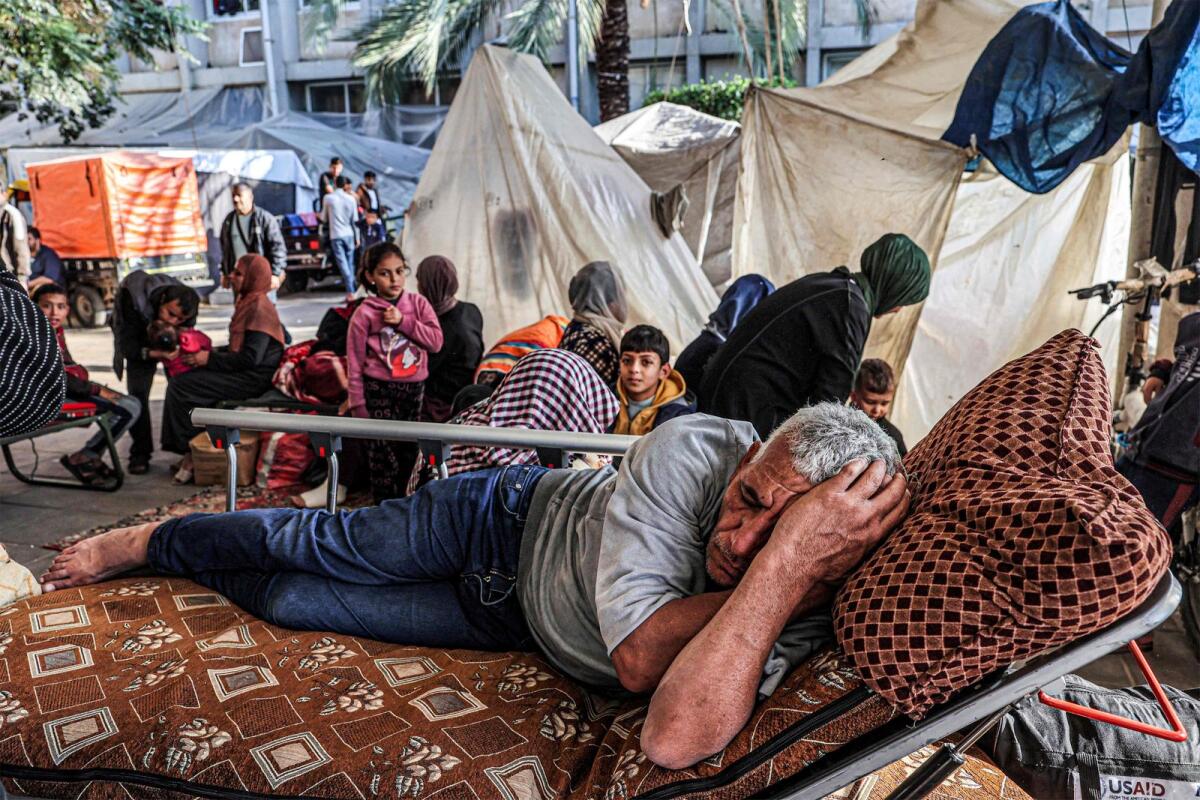 A man sleeps next to people sitting outside tents where displaced Palestinians are camped outside the European Hospital in Khan Yunis in the southern Gaza Strip on Monday. — AFP