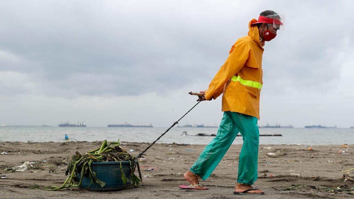 A worker wearing protective mask  pulls a plastic container full of debris washed ashore after tropical storm Saudel, locally called Pepito, hit the country on October 21, 2020 in Manila, Philippines.