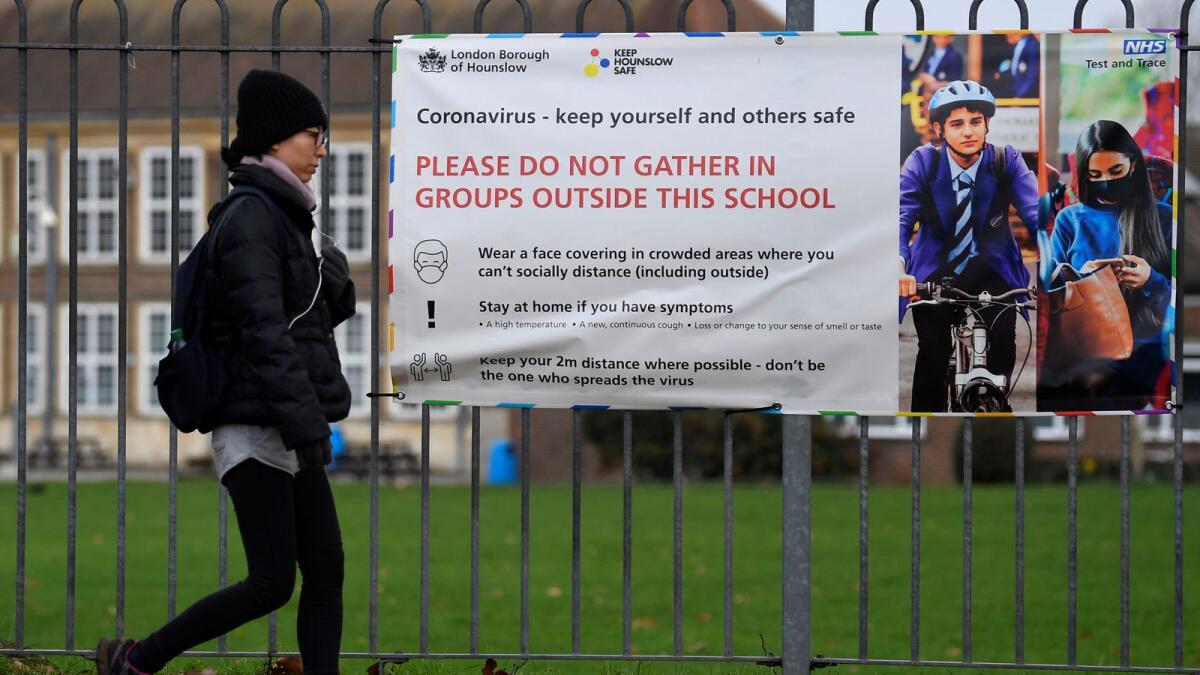 A woman walks past a social distancing health message outside of a secondary school in London on Wednesday.