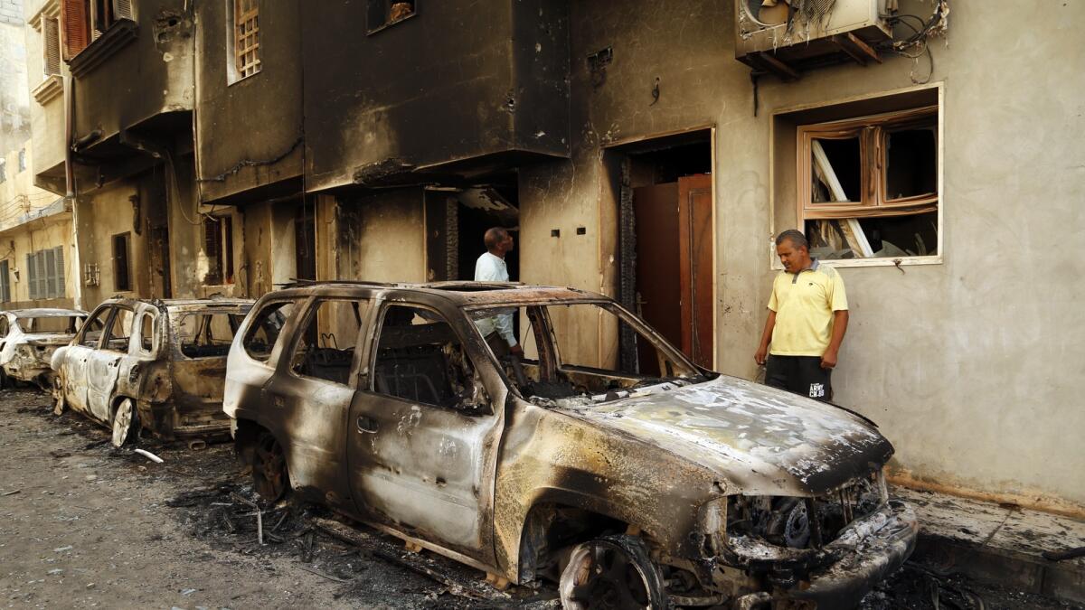 Men survey the remains of cars burned during clashes on a street in the Libyan capital of Tripoli. — AP