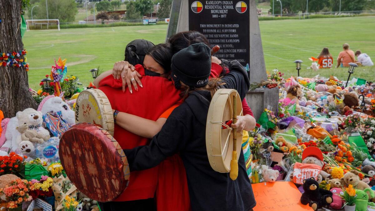 People from the Mosakahiken Cree Nation hug in front of a makeshift memorial at the former Kamloops Indian Residential School to honour the 215 children whose remains have been discovered buried near the facility, in Kamloops, British Columbia, Canada.