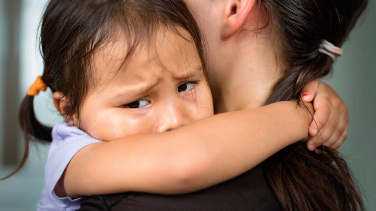 A sad child holding her mother for comfort and safety.