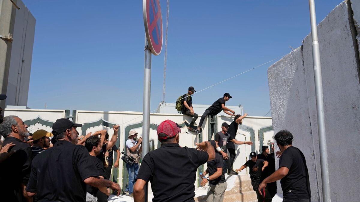 Supporters of Shia cleric Muqtada Al Sadr topple a concrete barrier in the Green Zone area of Baghdad, Iraq, on Monday. — AP