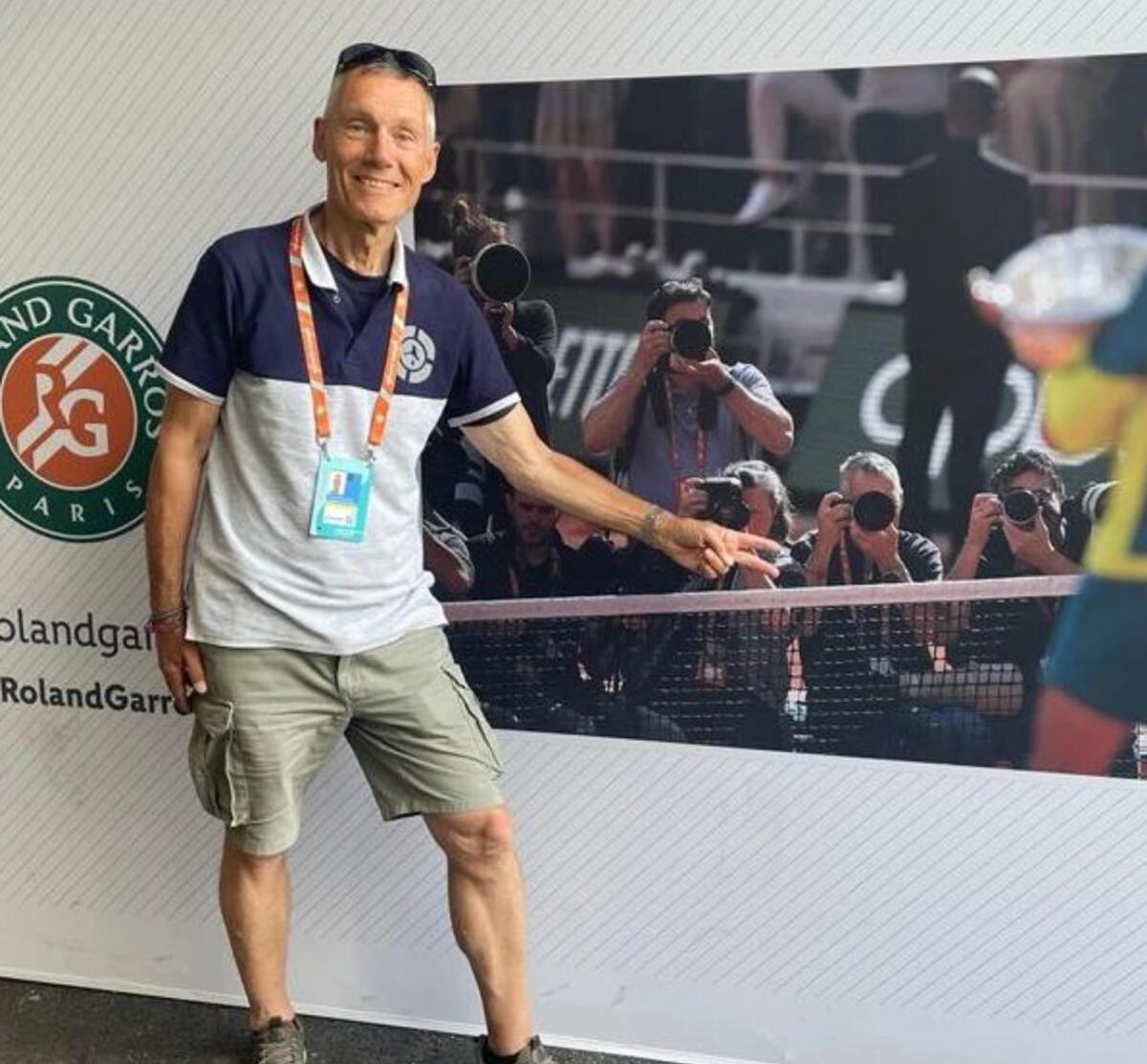 Hasenkopf is posing in front of a photograph at the French Open. In the picture, he is in the front row alongside other photographers, taking photos of the prize ceremony after the final