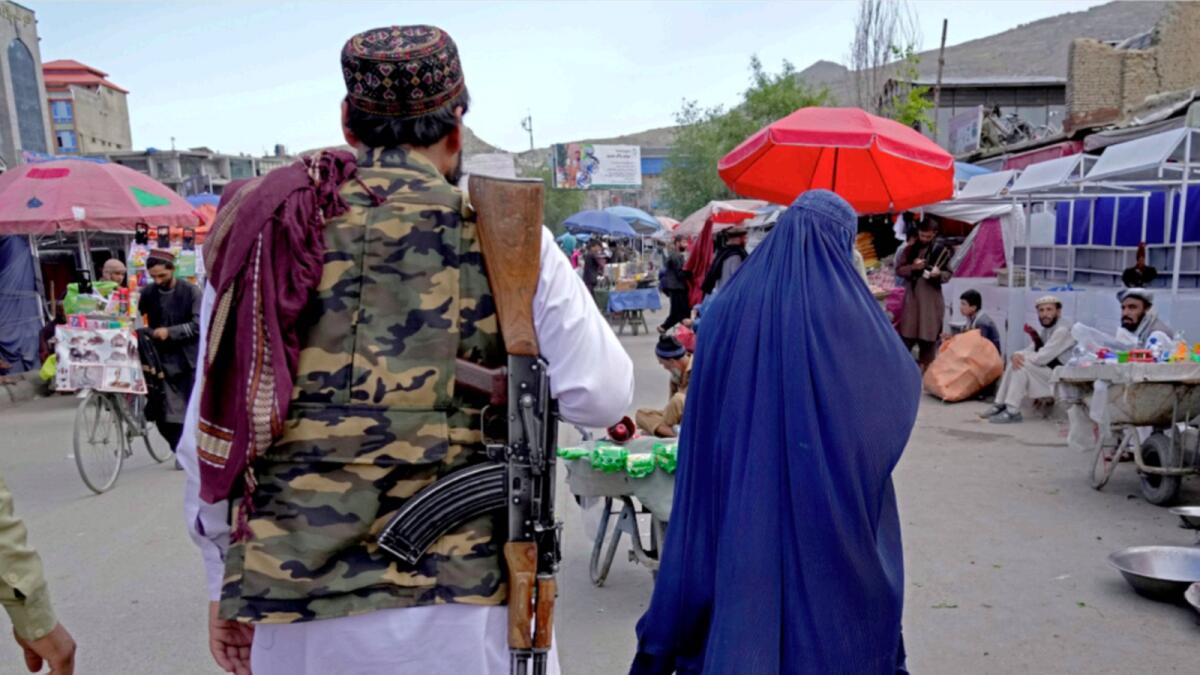 A woman wearing a burka walks through the old market as a Taliban fighter stands guard, in downtown Kabul. — AP