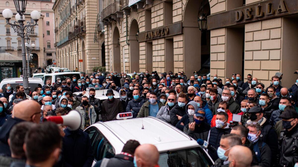 Taxi drivers wearing face masks stand next to taxis parked on Piazza Castello square in Turin, Italy, on Monday during a strike to protest against Covid-19 restrictions.