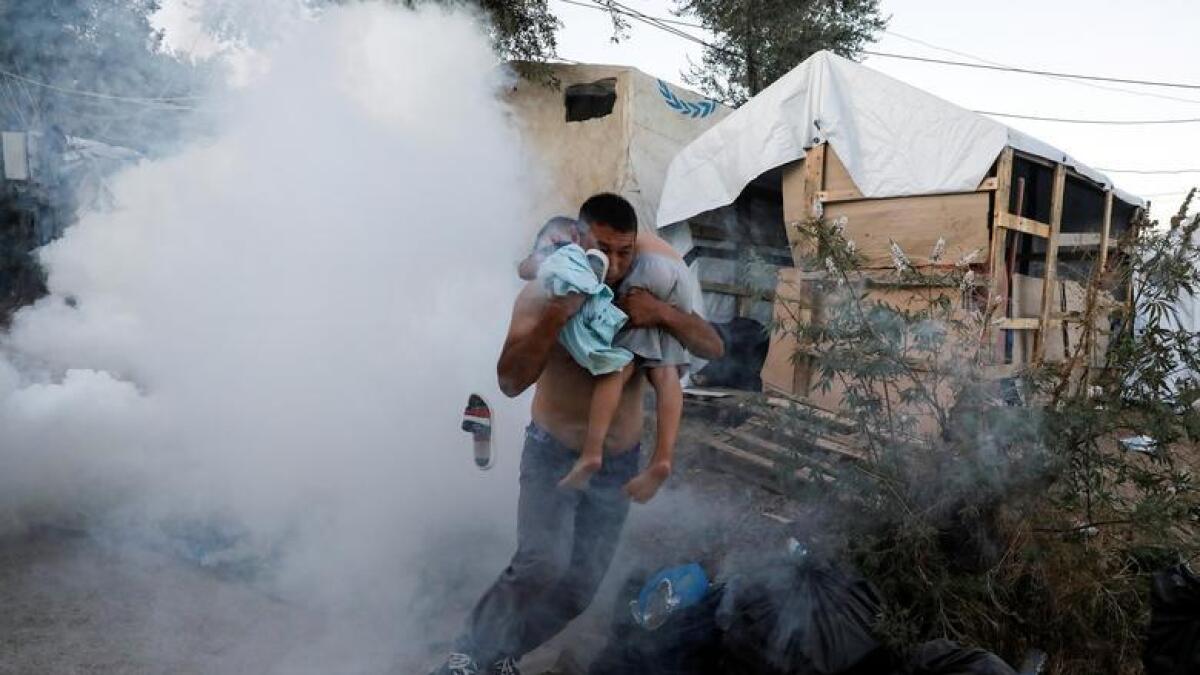 A migrant carries a boy as they flee tear gas fired by riot police during a demonstration, following a fire in Moria camp on the island of Lesbos, Greece, September 29, 2019. Reuters