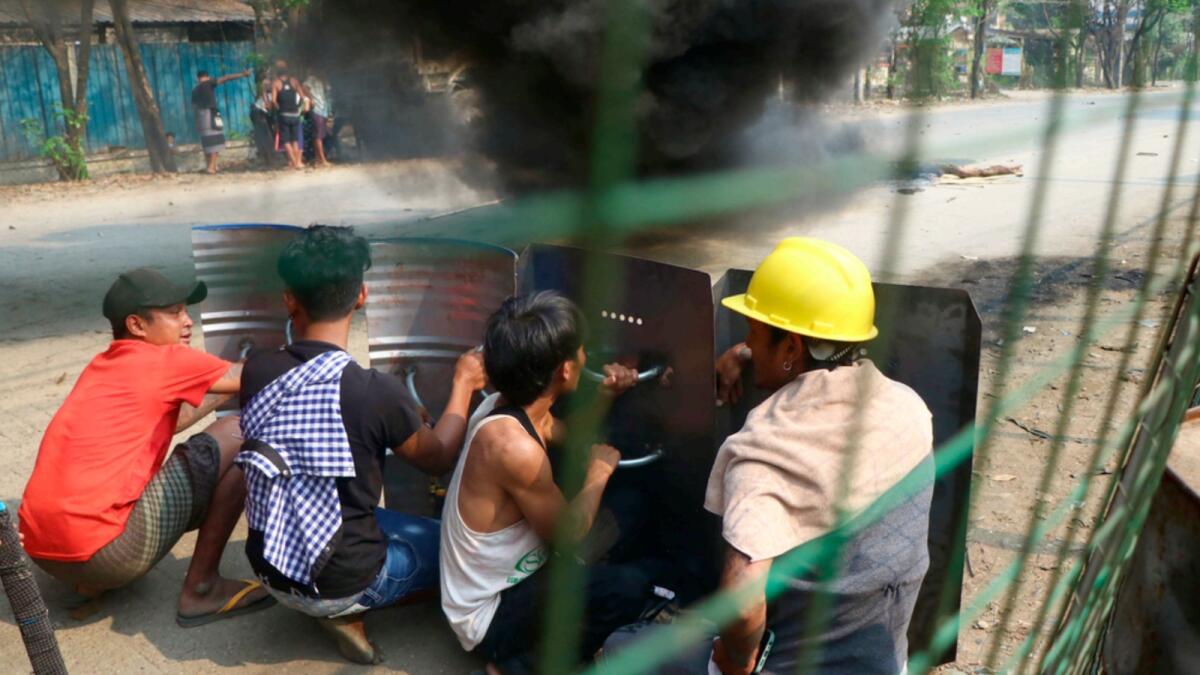 Anti-coup protesters squat with shields behind black smoke from burning debris on the road in Hlaing Tharyar township in Yangon. — AP file