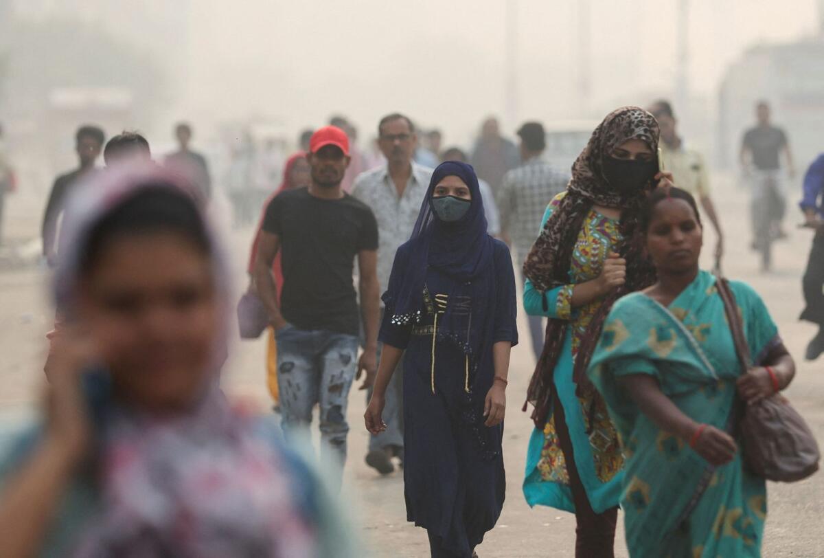 A woman with a facemask and other people walk amid the morning smog in New Delhi on Wednesday. — Reuters