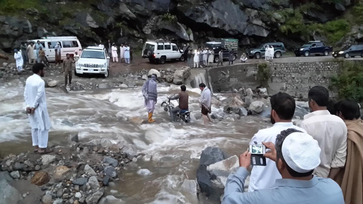 People standing on a road washed away by heavy flooding in Chitral, Pakistan
