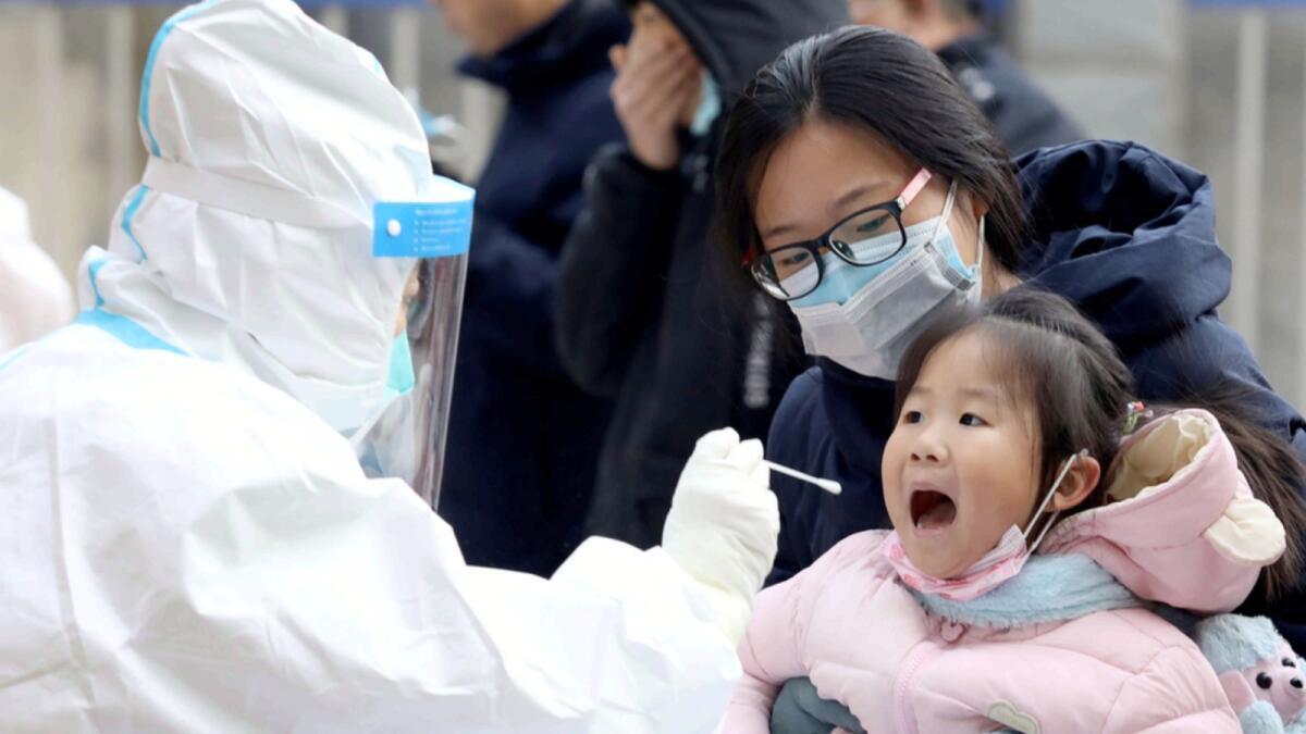 A worker in a protective suit takes a swab from a child for a coronavirus test in Shijiazhuang in northern China's Hebei Province. — AP
