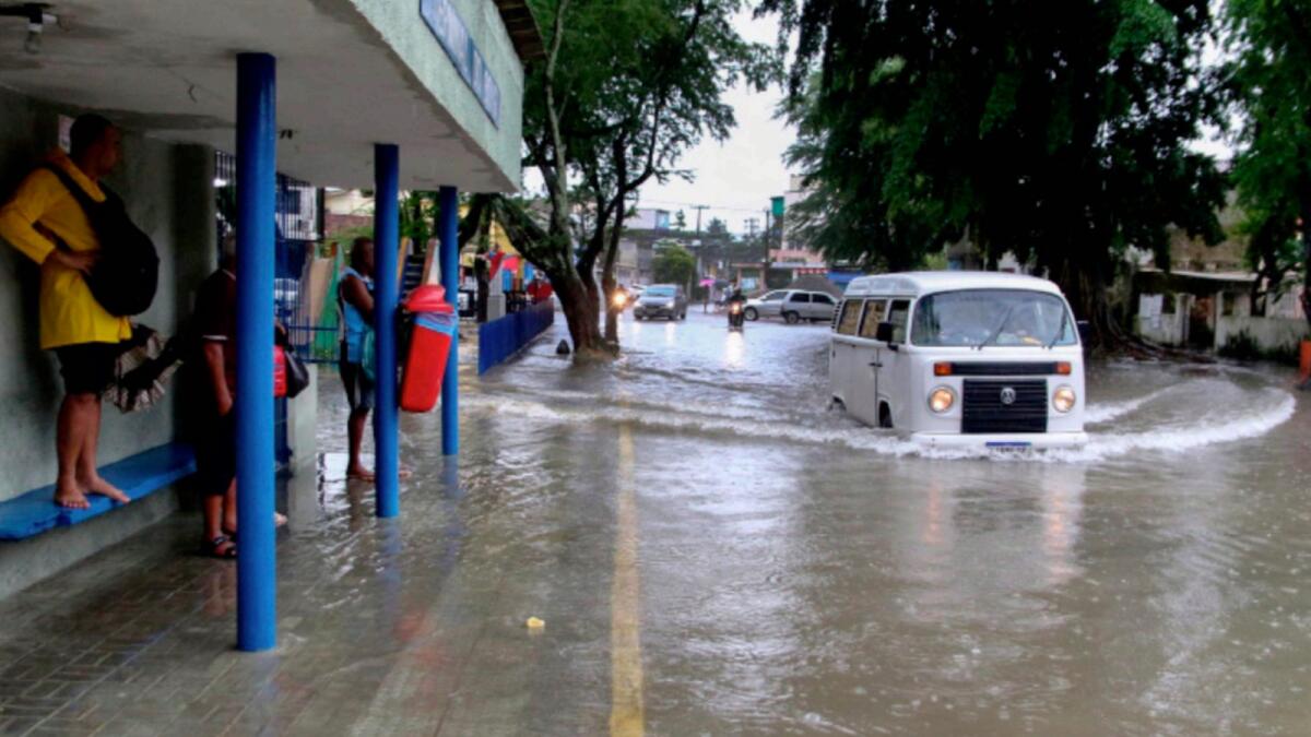 A woman stands on a bus stop bench as a driver of a van navigates a flooded street in Recife. — AP