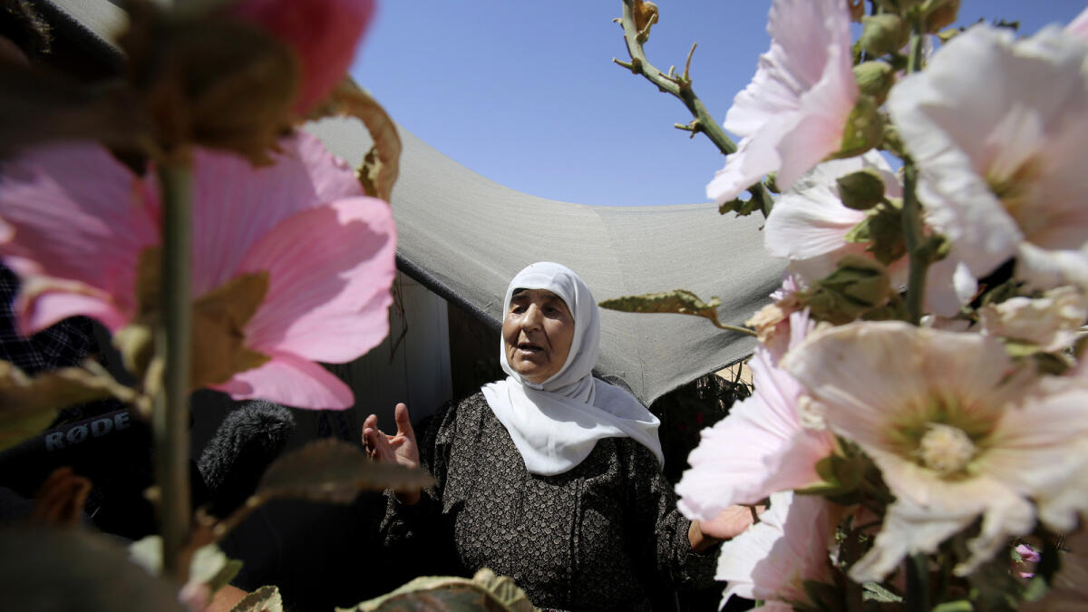 An elderly Syrian refugee woman stands outside her shelter surrounded with flowers she planted, at Zaatari refugee camp.