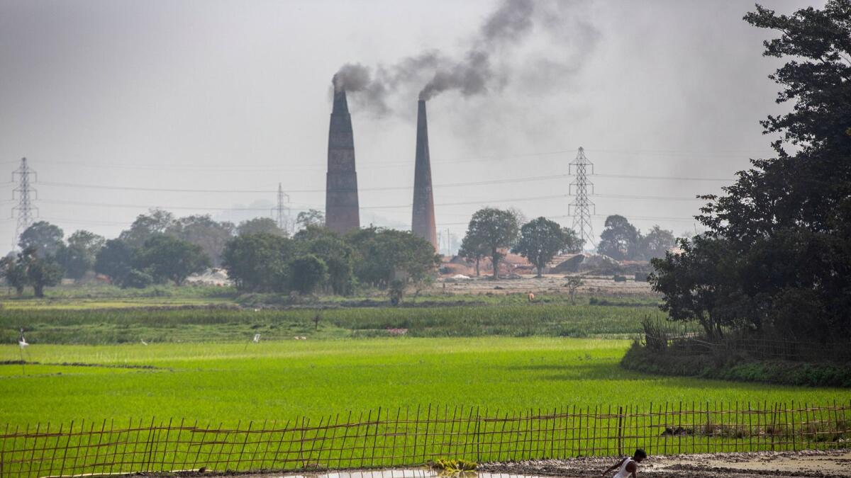 A farmer works in his paddy field as smoke rises from brick kilns on the outskirts of Gauhati, India. India's economy contracted by 7.7 per cent in the 2020-21 financial year, battered by the coronavirus pandemic, according to a report released on Friday. Agriculture remained the silver lining with 3.4 per cent growth, the report said. — AP