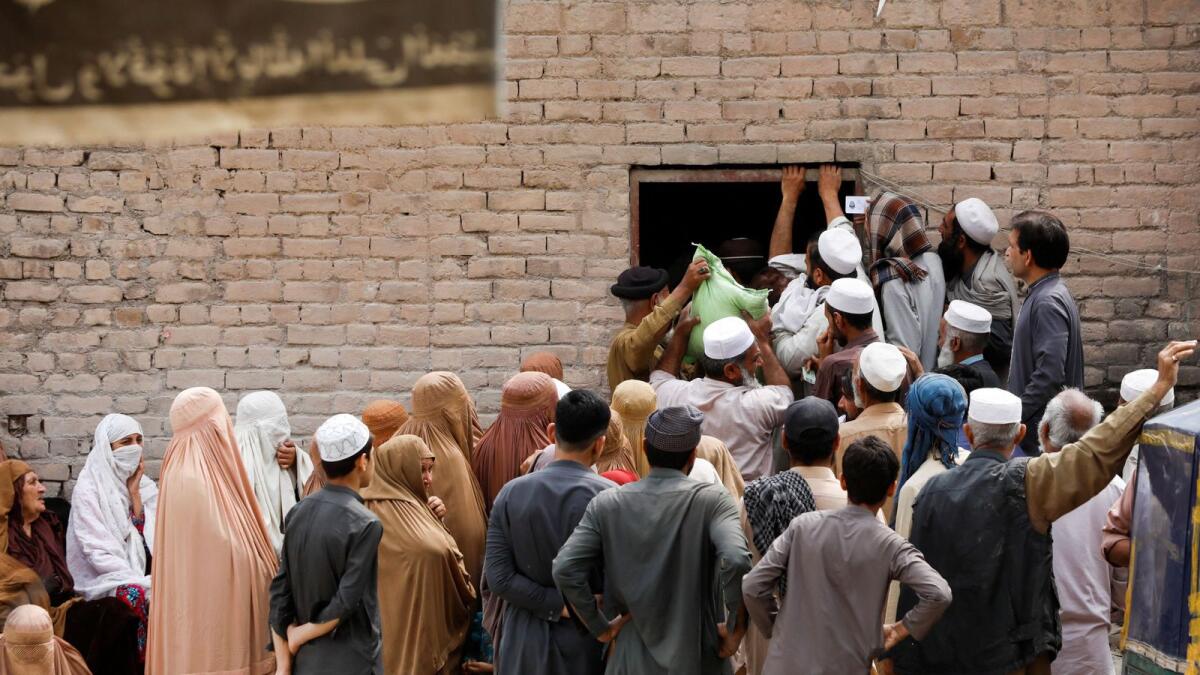 People gather to receive sacks of free flour at a distribution point in Peshawar, Pakistan, on Thursday. — Reuters