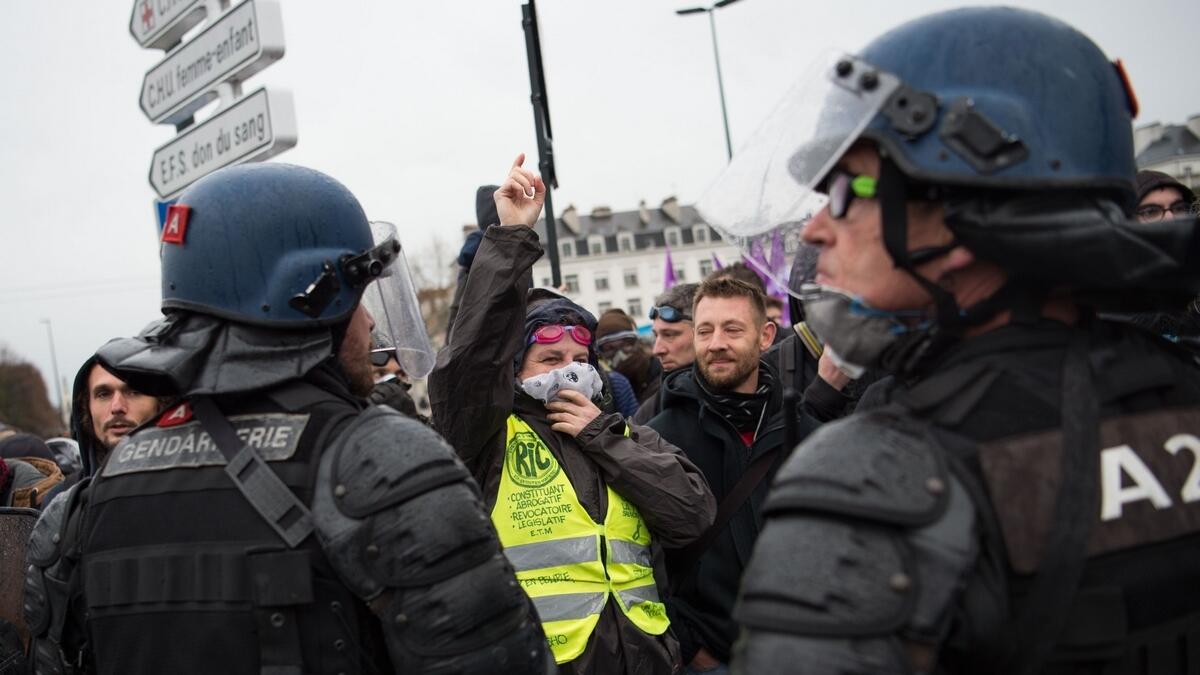 A woman wearing a yellow vest gestures in front of French gendarmes as people take part in a demonstration in Nantes on December 17, 2019 to protest against French government's plan to overhaul the country's retirement system, as part of a national general strike. Tens of thousands of protesters prepared to hit streets across France over a pensions overhaul that has sparked a crippling transport strike, though government officials insist they will not give in to union demands they drop the plan.  AFP